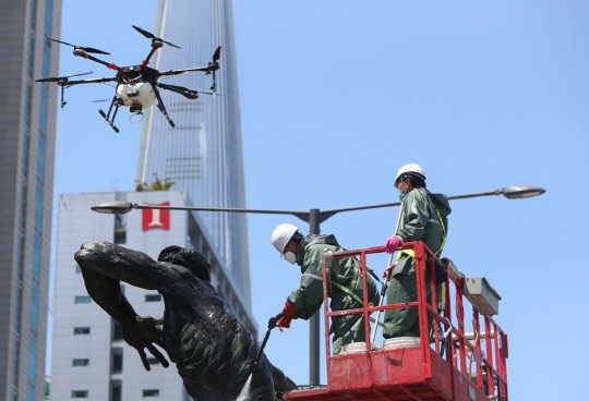 서울 송파구 올림픽로에서 구청 관계자들이 드론과 고압 세척기를 이용해 올림픽 상징 조형물을 세척하고 있다.<연합뉴스>